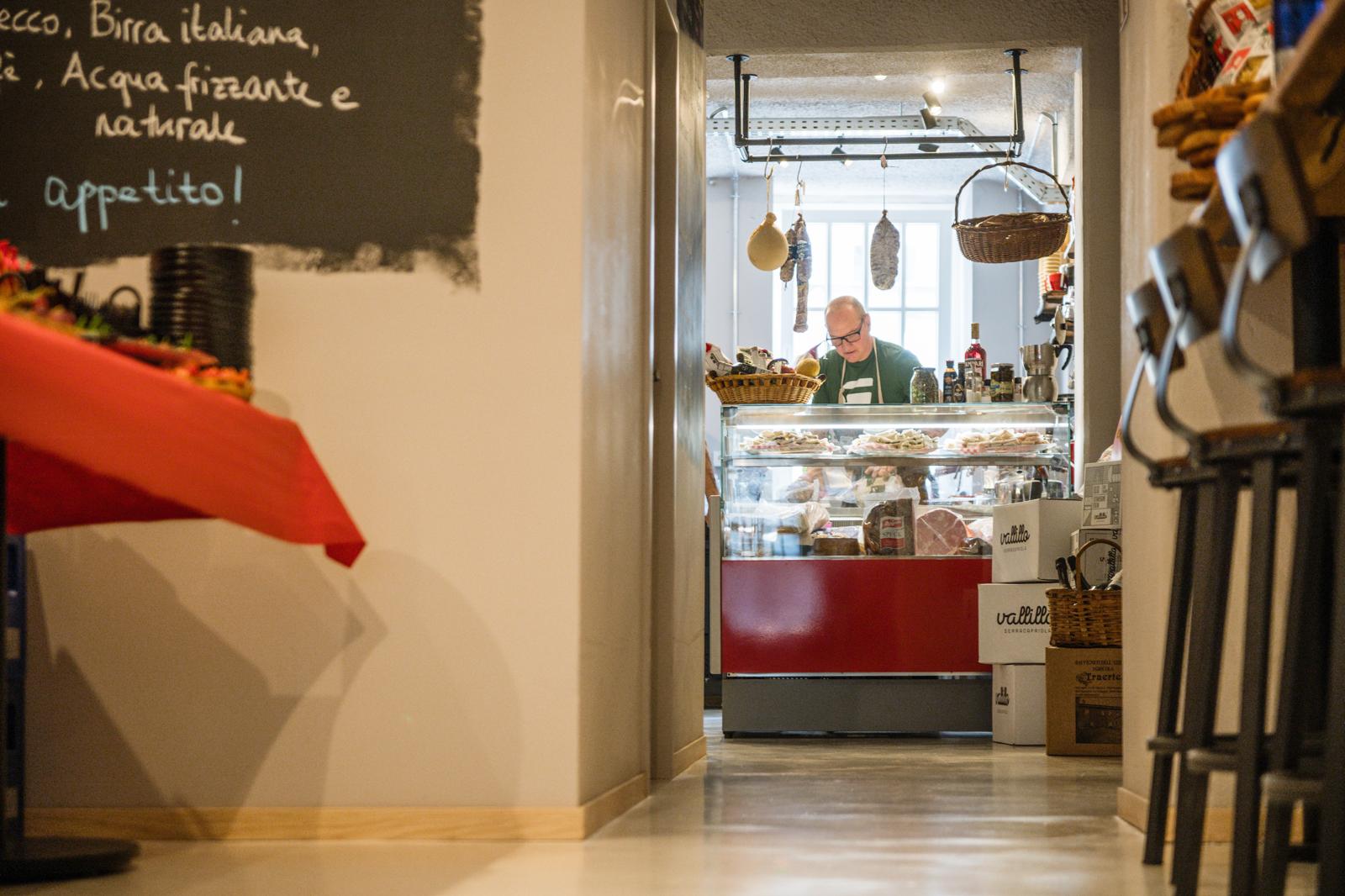 Blick durch den Eingang in das Verace — Andrea an der Feinkosttheke, Tafel mit Tagesangeboten an der Wand
